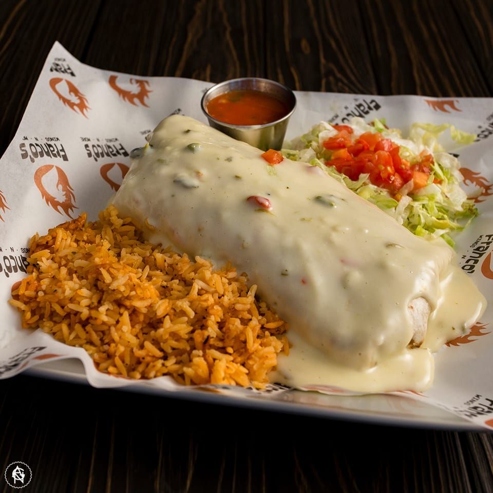 A Franco's Wings N More burrito covered in white cheese sauce, with rice, lettuce, and diced tomatoes.