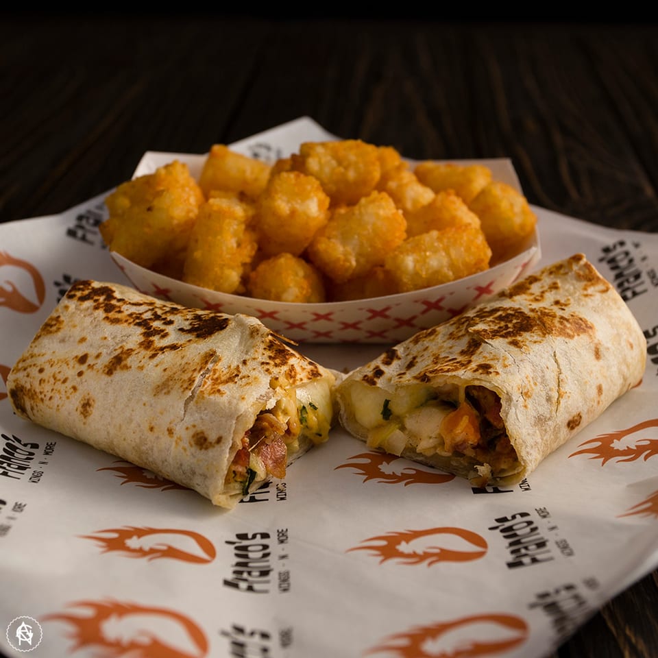 Two Franco's burritos, one cut in half, with a side of golden tater tots on branded paper.