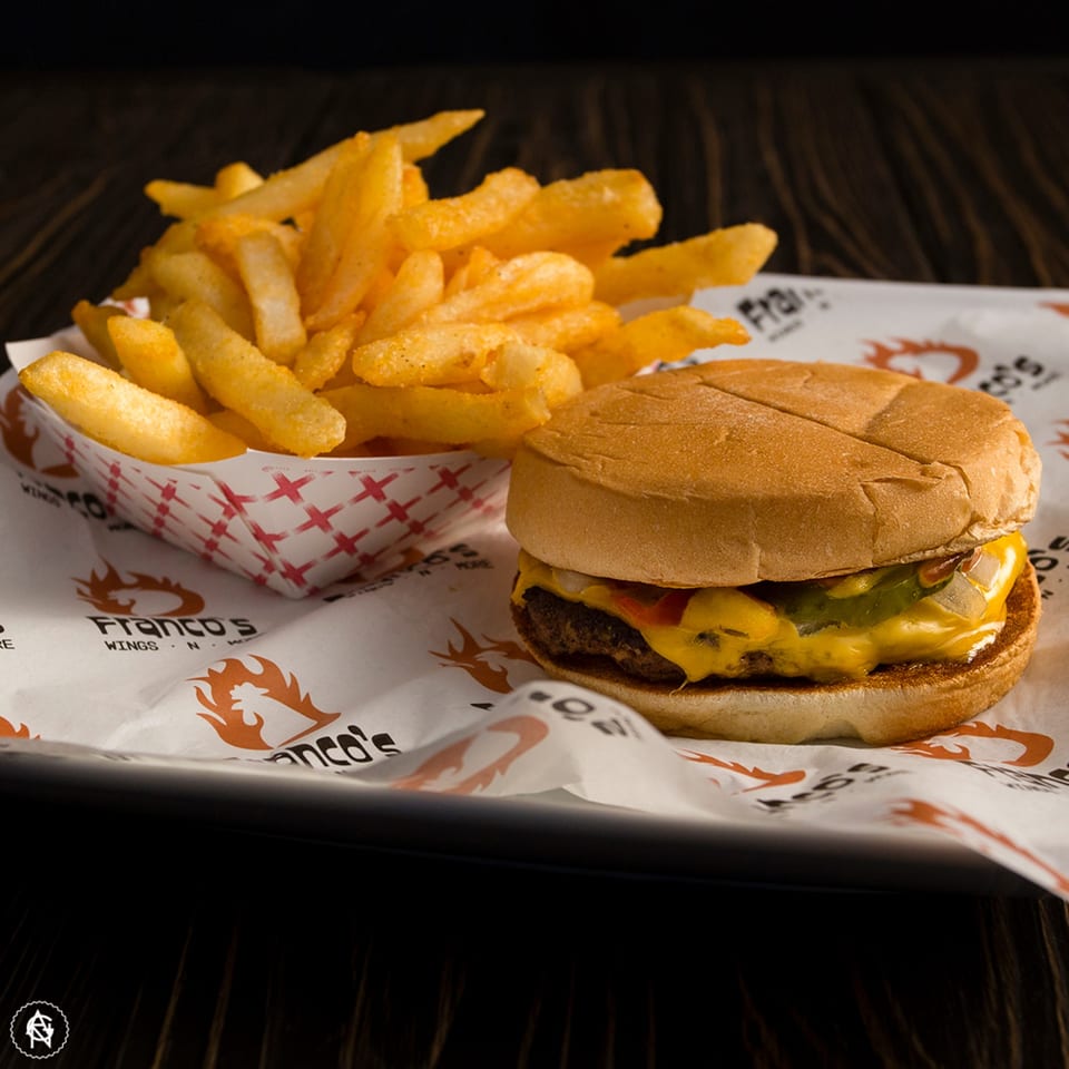 A Franco's cheeseburger with melted cheese and pickles, next to a container of golden fries.